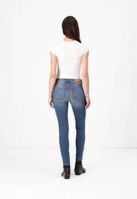 Jeans ajustados en denim azul medio con un ligero desgaste, que presentan un diseño tradicional de cinco bolsillos y una etiqueta de cuero con marca en la parte trasera.