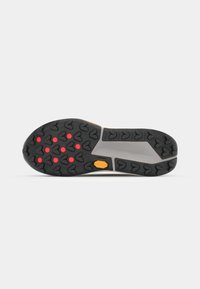 Semelle de chaussure en caoutchouc noir avec des motifs de traction en forme de flèche et six grips circulaires rouges sur l'avant-pied, ainsi qu'un logo Vibram jaune près de la voûte plantaire.
