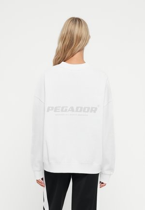 Sudadera blanca de gran tamaño con hombros caídos, puños y dobladillo acanalados. Presenta un logo en gris en la parte posterior. Tejido suave de mezcla de algodón.
