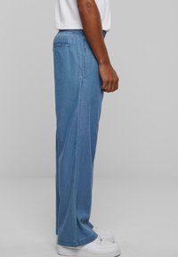 Løse blå denimbukser med elastisk talje, sidelommer og lige ben, parret med hvide sneakers.