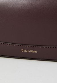 Burgunderfarbenes Kunstlederportemonnaie mit glatter Textur. Mit goldenem "Calvin Klein"-Logo und einer Naht entlang der Kante.