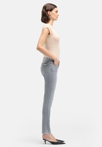 Jasnoszare obcisłe dżinsy o gładkiej fakturze, zestawione z dopasowanym beżowym topem i czarnymi spiczastymi szpilkami, widoczne z boku.