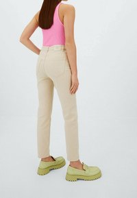 Beige korkeavyötäröiset farkut, joissa on slim fit -leikkaus, yhdistettynä vaaleanvihreisiin korkokenkiin, joissa on nauha-akcentti. Mallilla on yllään vaaleanpunainen toppi.