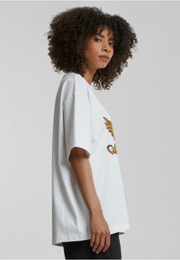 Hvit bomull oversized t-skjorte med korte ermer og et buet grafisk design i gul-oransje over brystet, med en avslappet silhuett.