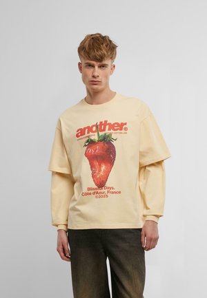 T-shirt en coton jaune clair avec un grand motif de fraise, texte rouge en bold et coupe ample et décontractée.
