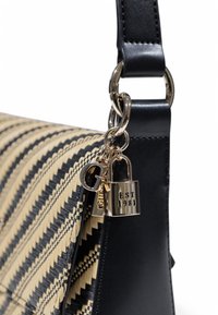 Sac à main tissé noir et beige avec un motif en zigzag, une bandoulière en cuir et des accessoires métalliques avec un détail de verrouillage et un charme.