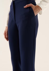 Námořnické modré kalhoty na míru vyrobené z hladkého materiálu, s boční kapsou, štíhlým siluetou a zapínáním na zip v přední části.