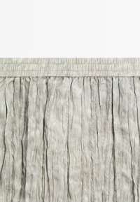 Tissu gris clair plissé avec une ceinture élastique froncée. La surface texturée crée des lignes verticales, offrant un aspect doux et fluide.