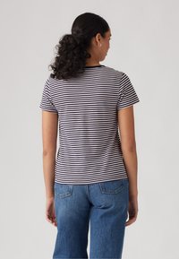 Camiseta de rayas en azul marino y blanco, de manga corta, cuello redondo, forma ligeramente ajustada, hecha de algodón suave. Combinada con jeans azules.
