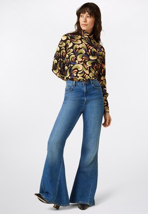Langdurige blouse met een draaitend meerkleurig patroon, gecombineerd met hoge taille flared blauwe jeans. Glad materiaal en getailleerd ontwerp.