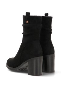 Botas negras de tobillo holgadas, hechas de suave ante, con punta redonda y un tacón grueso, con un pequeño acento dorado en la parte posterior.