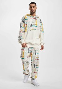 Cream hooded sweatshirt with colorful "DNGRS" print, paired with matching pants in the same pattern. White sneakers complete the outfit.