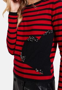 Rot- und schwarz gestreifter Pullover mit einem schwarzen Herzdesign, das mit Strasssteinen verziert ist. Er verfügt über einen gerippten Halsausschnitt und Rippbündchen.