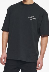 Černé bavlněné tričko s krátkým rukávem, na levé straně hrudi s malým bílým vyšitým textem "CITY OF ANGELS".