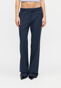 Παντελόνια σε ναυτικό μπλε, με ευθύ σχεδιασμό, κρίκους για ζώνη και μπροστινές τσέπες. Λείο ύφασμα με ελαφριά γυαλάδα και καθαρό φινίρισμα.