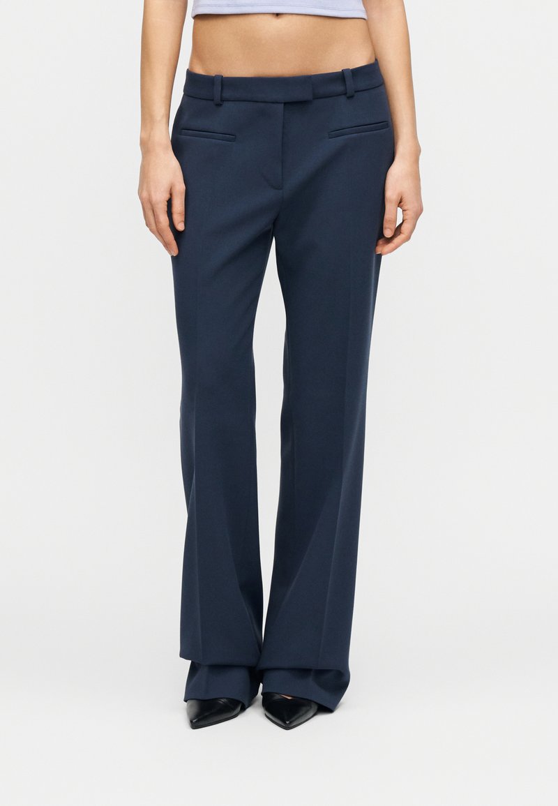 Παντελόνια σε ναυτικό μπλε, με ευθύ σχεδιασμό, κρίκους για ζώνη και μπροστινές τσέπες. Λείο ύφασμα με ελαφριά γυαλάδα και καθαρό φινίρισμα.