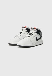 Αθλητικά παπούτσια μέσου ύψους με λευκό επάνω μέρος από δέρμα, μαύρες λεπτομέρειες και κόκκινες πινελιές. Διάτρητη μύτη, λαστιχένια σόλα με σχέδιο πρόσφυσης και λευκά κορδόνια.