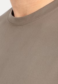 Koszula z krótkim rękawem w jasnobrązowym kolorze, wykonana z miękkiej tkaniny o gładkiej teksturze. Posiada okrągły dekolt i przeszycia wokół kołnierza.