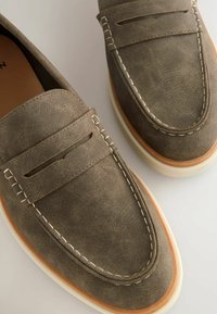Grå ruskinds loafers med hvid kontrastsyning, slip-on design og en tekstureret overdel med en glat, rund tå.