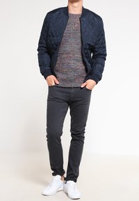 Chaqueta bomber acolchada azul marino sobre un suéter de punto multicolor, combinada con jeans negros ajustados y zapatillas blancas.