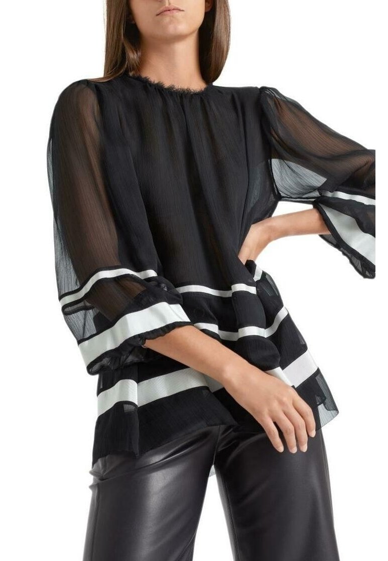 Blouse noire transparente avec des manches évasées, présentant des rayures blanches horizontales aux poignets et à l'ourlet. Tissu léger et texturé avec une coupe ample.