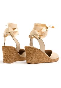 Beżowe espadryle na koturnie z plecioną, jutową podeszwą, z gładkim materiałowym wierzchem i satynowymi wstążkami związanymi w kostce.