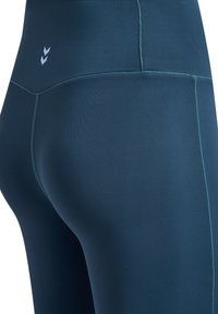 Teal träningsleggings med hög midja, slät textur och kontrasterande sömmar, som visar upp en stilren design.