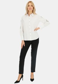 Biała koszula zapinana na guziki z długimi rękawami, ozdobiona gwiazdkami na ramionach, z klasycznym kołnierzykiem, w połączeniu z czarnymi dopasowanymi spodniami.