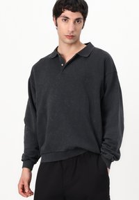 Dark gray long-sleeve polo shirt with a collared neck and subtle logo on the chest. Soft texture and relaxed fit. Wrinkled fabric appearance.
