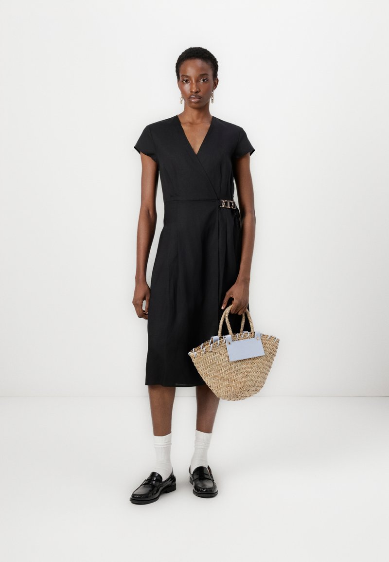 Czarna sukienka o kroju kopertowym z krótkimi rękawami, z dodatkowym detalem w postaci klamry z boku. Połączona z plecioną torbą ze słomy i czarnymi mokasynami noszonymi z białymi skarpetkami.