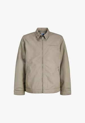 Világos barna, cipzáras dzseki gallérral, két oldalsó zsebbel és egy varrt mellzsebbel, fehér háttér előtt bemutatva.