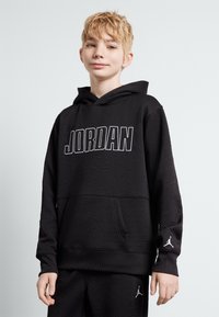 Černá mikina s kapucí s texturovaným geometrickým vzorem, s nápisem "JORDAN" v bílé barvě a malým logem na levém rukávu.