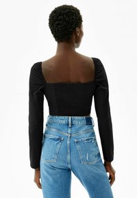 Svart figursydd topp med lång ärm och fyrkantig halsringning, kombinerad med högmidjade blå denimjeans med slitna detaljer.