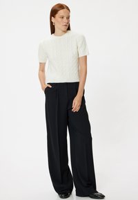 Suéter blanco de punto con mangas cortas y patrón texturizado, combinado con pantalones de pierna ancha negros de talle alto, que presentan una silueta relajada.