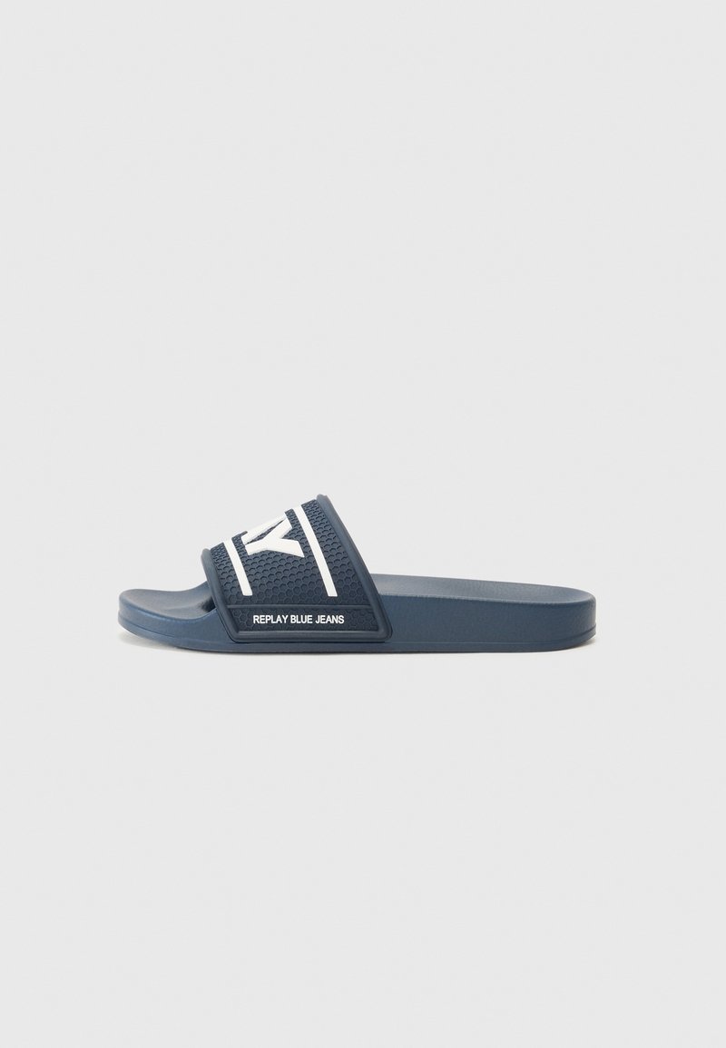 Mules en caoutchouc bleu marine avec un dessus texturé et un logo blanc contrastant. Semelle plate avec une large sangle pour le confort et la stabilité.