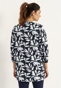 Floral tunic featuring a black background with white and light blue leaf patterns, long sleeves with elastic cuffs, and a rounded hem.