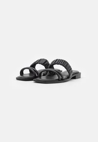 Zwarte platte sandalen met twee brede, samengevoegde banden en een platte zool. Het materiaal lijkt glad met een subtiele glans.