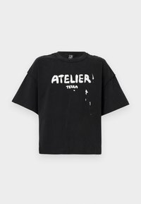 Črna bombažna majica s prevelikim krojem, kratkimi rokavi, okroglim izrezom in belim grafičnim besedilom "ATELIER TERRA" z detajlom kapljanja, ki spominja na barvo.