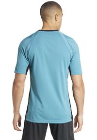 Maglietta sportiva blu con maniche corte, dettagli neri ai lati e scollatura rotonda; realizzata in tessuto liscio e traspirante.