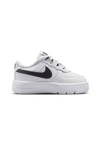 Λευκό αθλητικό παπούτσι χαμηλού προφίλ με μαύρο λογότυπο Nike, δέρμα με υφή, μαύρα και λευκά κορδόνια, και παχύ ελαστικό πέλμα, απεικονίζεται σε πλάγια όψη.