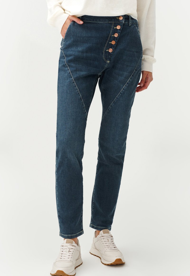 Dark blue denim jeans with a high waist, featuring a diagonal seam and five decorative buttons on the side. Smooth texture and slim fit.