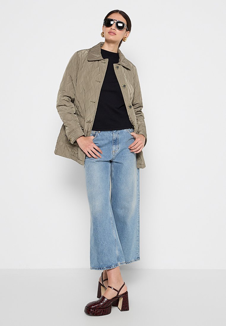 Khakifreie Jacke mit Steppung und Kragen, schwarzes enges Oberteil, hellblaue weite Jeans und dunkelburgunderfarbene Blockabsatzschuhe.