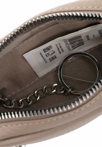 Interior de bolso de tela beige con cremallera plateada, enganche de cadena y etiqueta de cuidado. Textura suave con un diseño sencillo.
