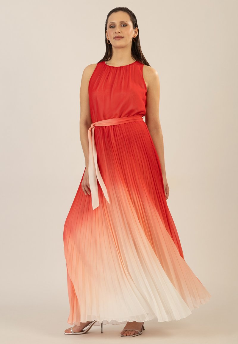 Robe longue plissée dégradée de rouge à blanc, sans manches, avec un col rond, dotée d'une ceinture à nouer à la taille et de talons argentés subtils.