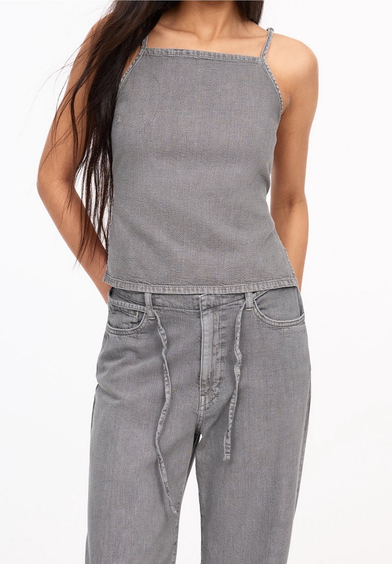 Haut en denim gris avec fines bretelles, encolure carrée et ourlet brut, associé à un pantalon gris assorti avec taille à cordon et poches.