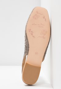 Beige shoe with a textured, sparkly upper and an embellished design. The sole features floral prints and a size indication of 37.