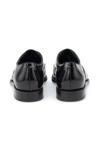 Chaussures en cuir verni noir avec une finition lisse et brillante. Présentent un petit talon et un design arrondi avec des détails sur le côté.
