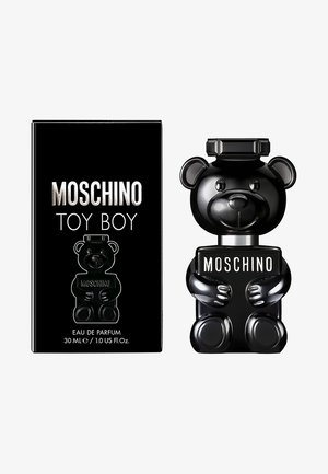 Flacon de parfum Black Moschino Toy Boy en forme d'ours tenant une plaque avec le texte « MOSCHINO », à côté de son emballage noir assorti.