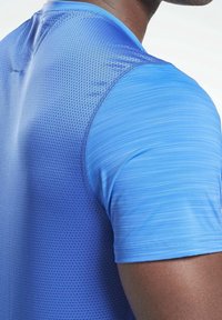 Blå idrottströja med en texturerad, andningsbar tyg på den övre delen, slät nedre del med subtila horisontella ränder.