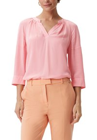 Rosa Bluse mit V-Ausschnitt, drei Viertelärmeln und gerafftem Stich am ausschnitt, kombiniert mit hellen pfirsichfarbenen, taillierten Hosen.